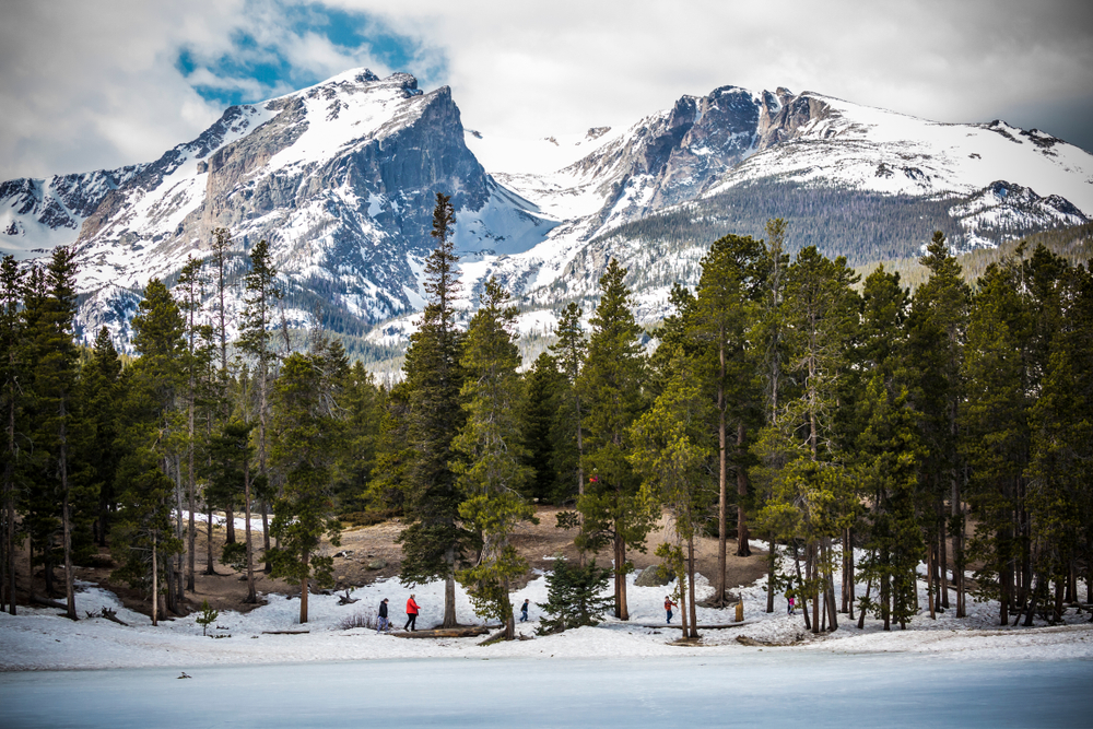 Landscape view of Rocky Mountains National Park in Colorado with trees in the foreground and mountains in the background.