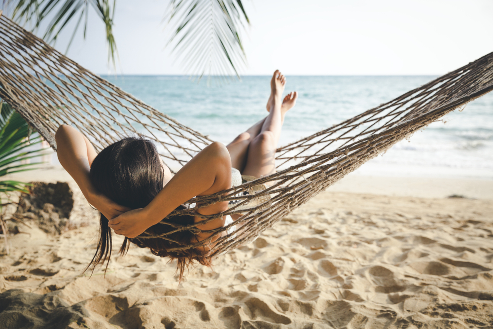 Happy woman relaxing in hammock on tropical beach at sunset.