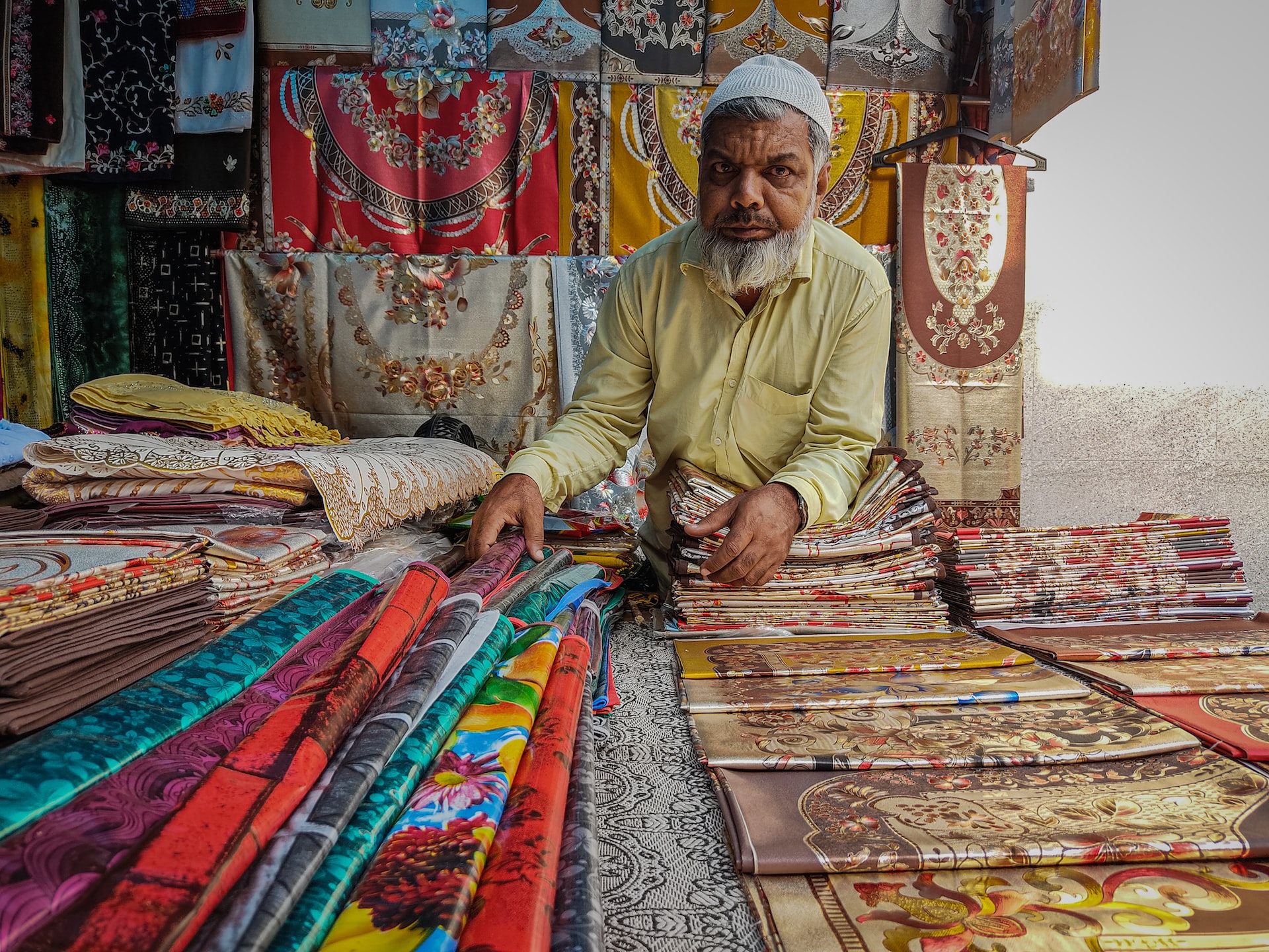 Man selling shawls in India out of storefront.