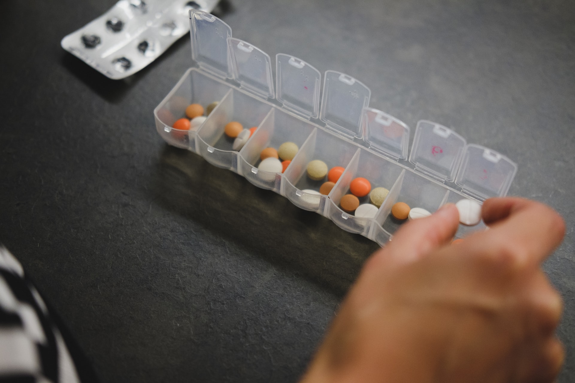 A hand arranging medications in a plastic carry case.