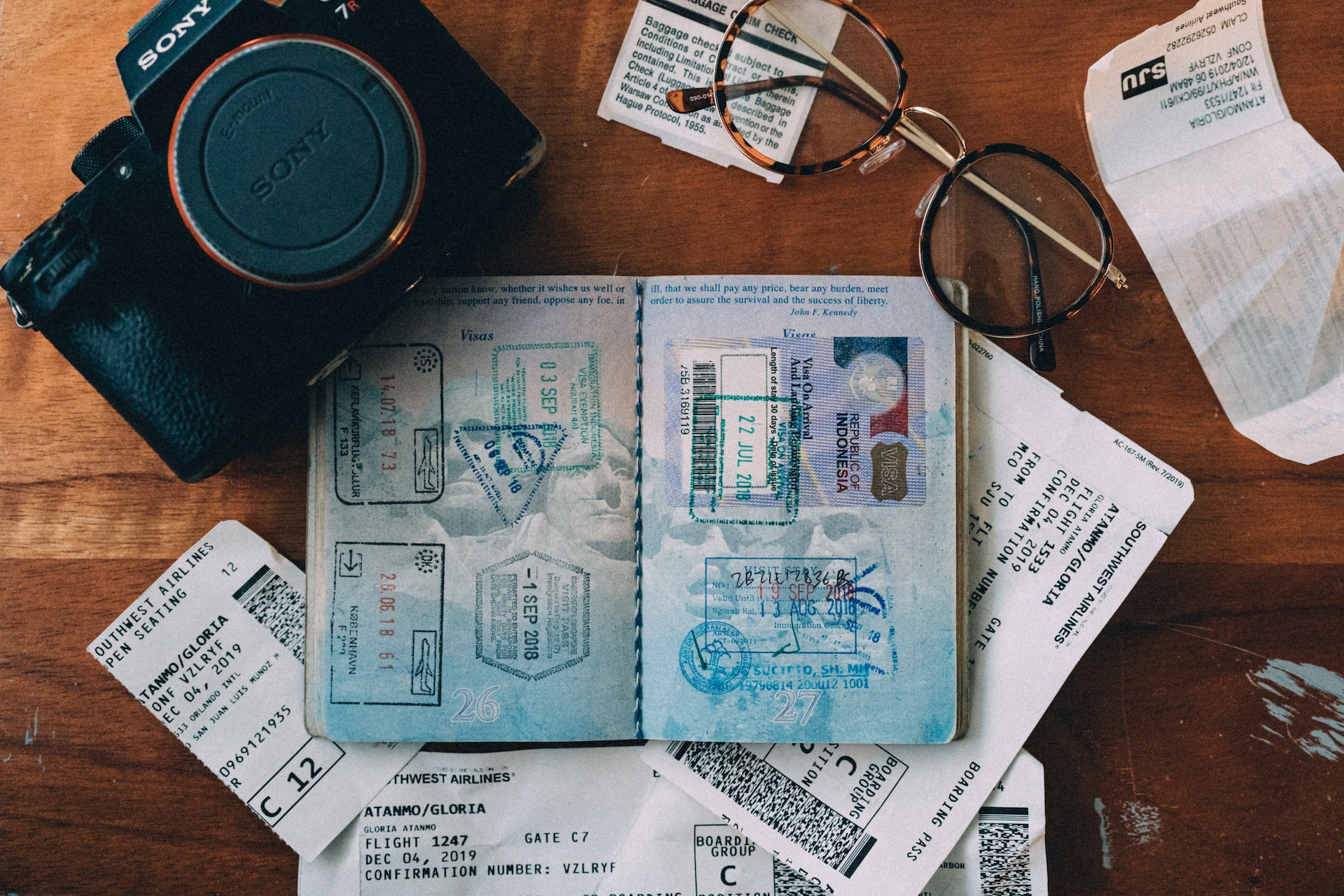 Items including an open passport and a camera arrayed on a wooden desk.