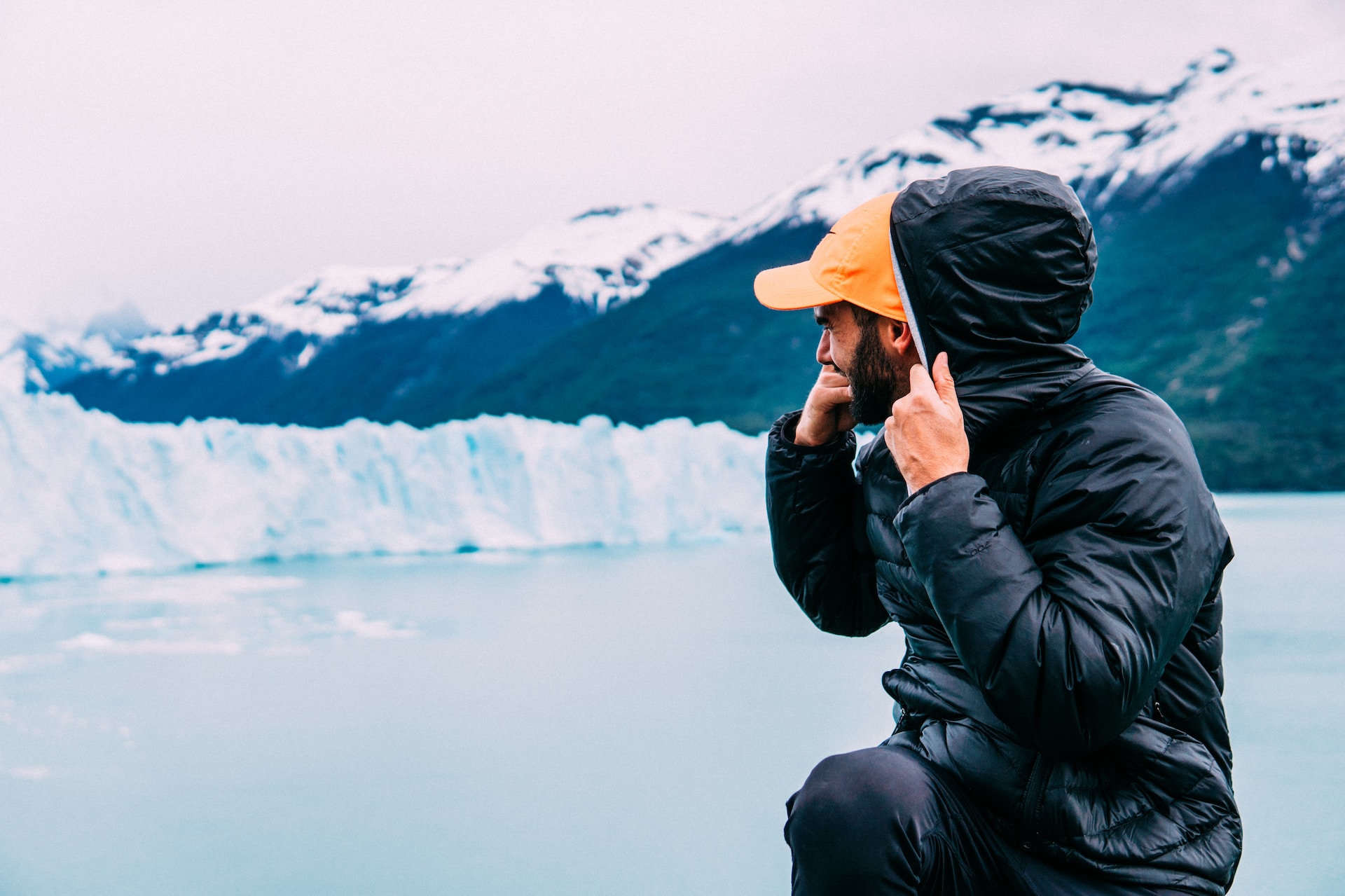 A man with his hoodie up staring at some glaciers.