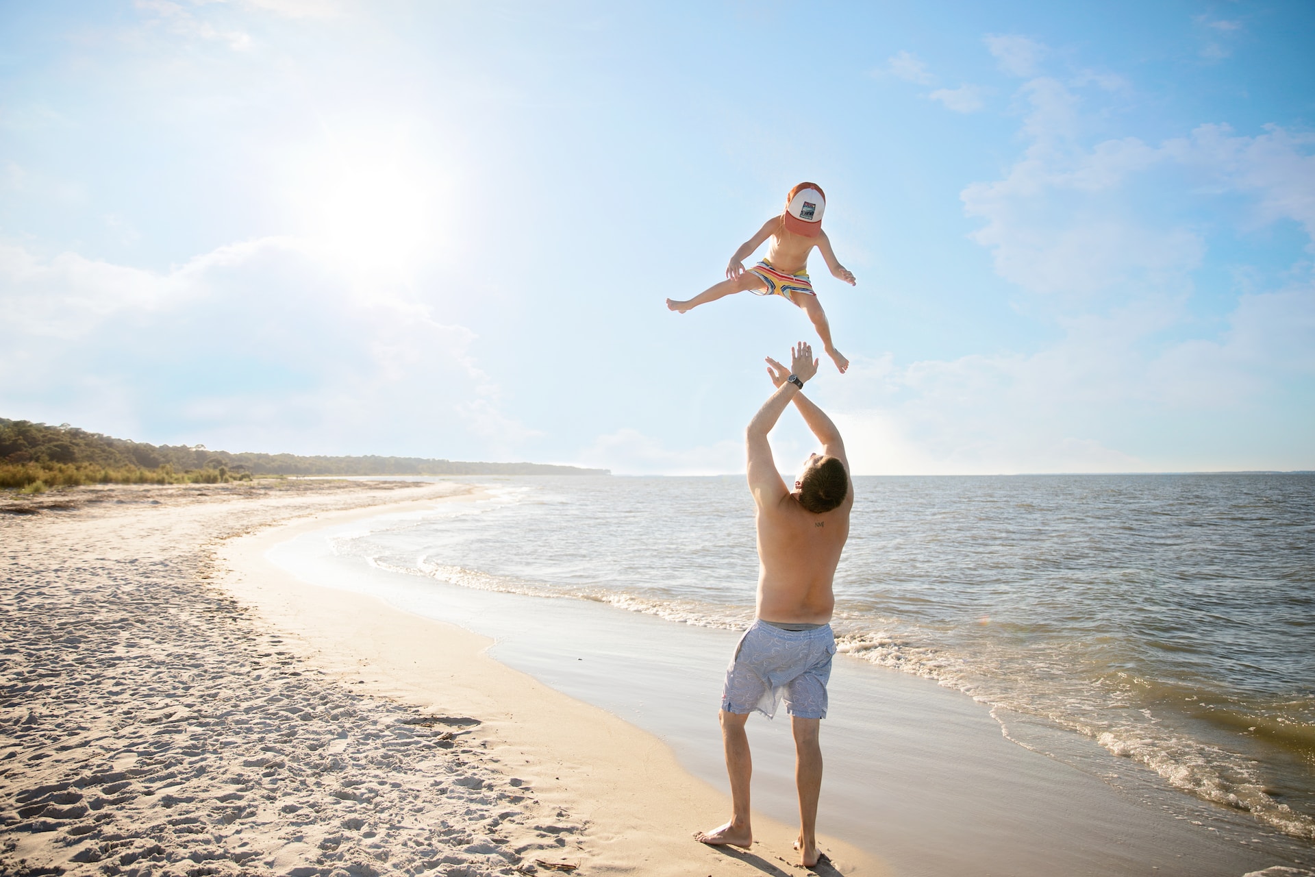 A dad tossing his son into the air at the beach.