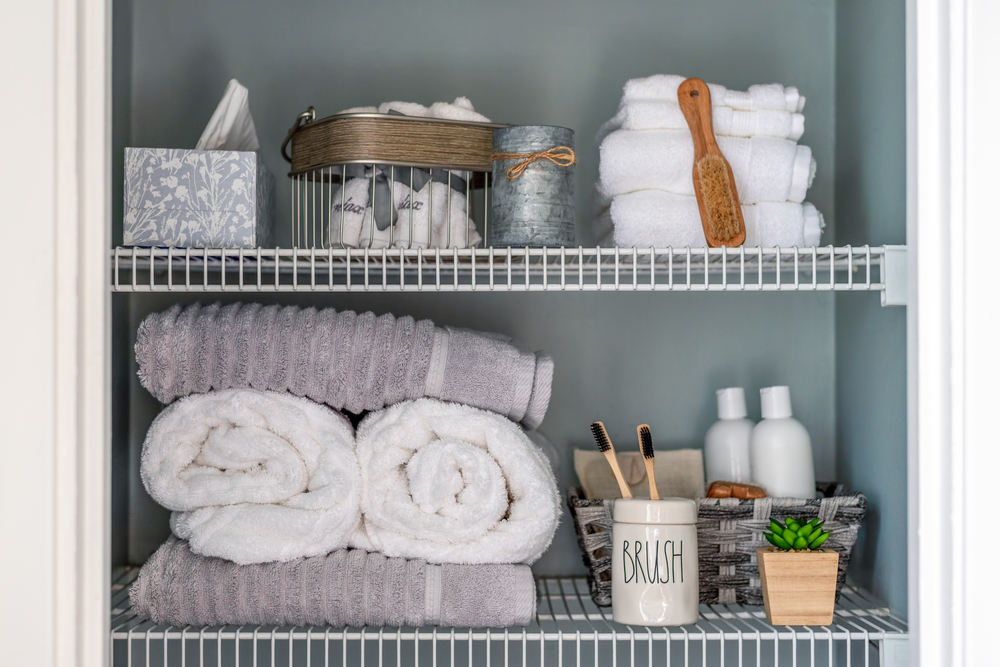 Neatly organized bathroom linen closet with bamboo toothbrushes and white towels.