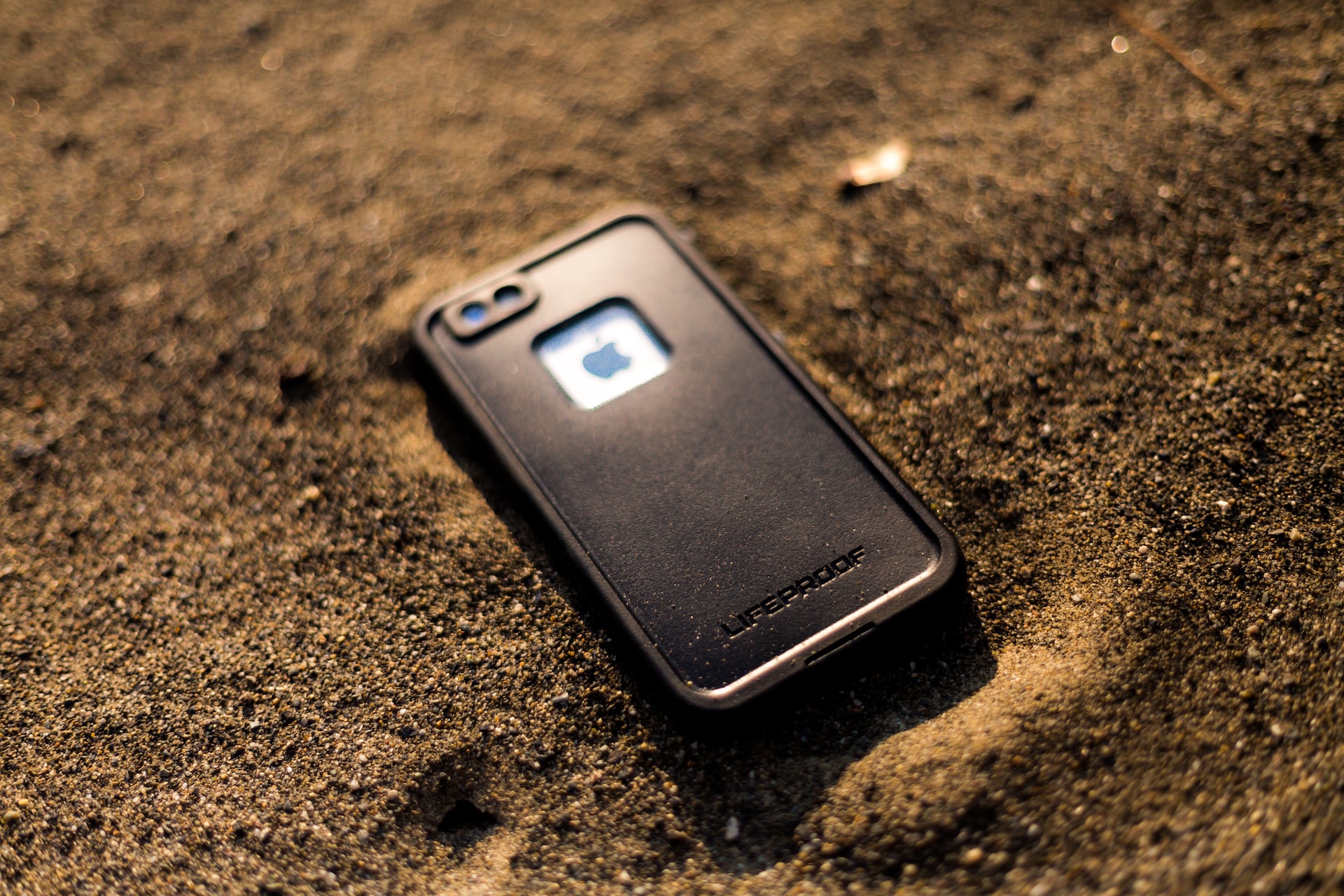 Phone in a waterproof case lying in the sand.