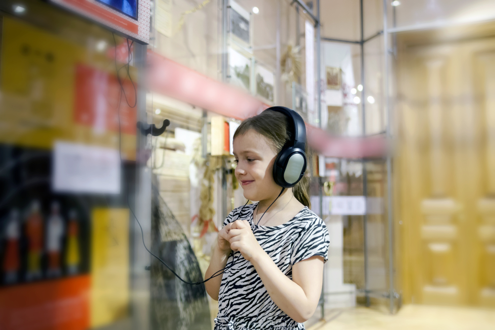 girl in museum listening to interesting information about exhibit through headphones.