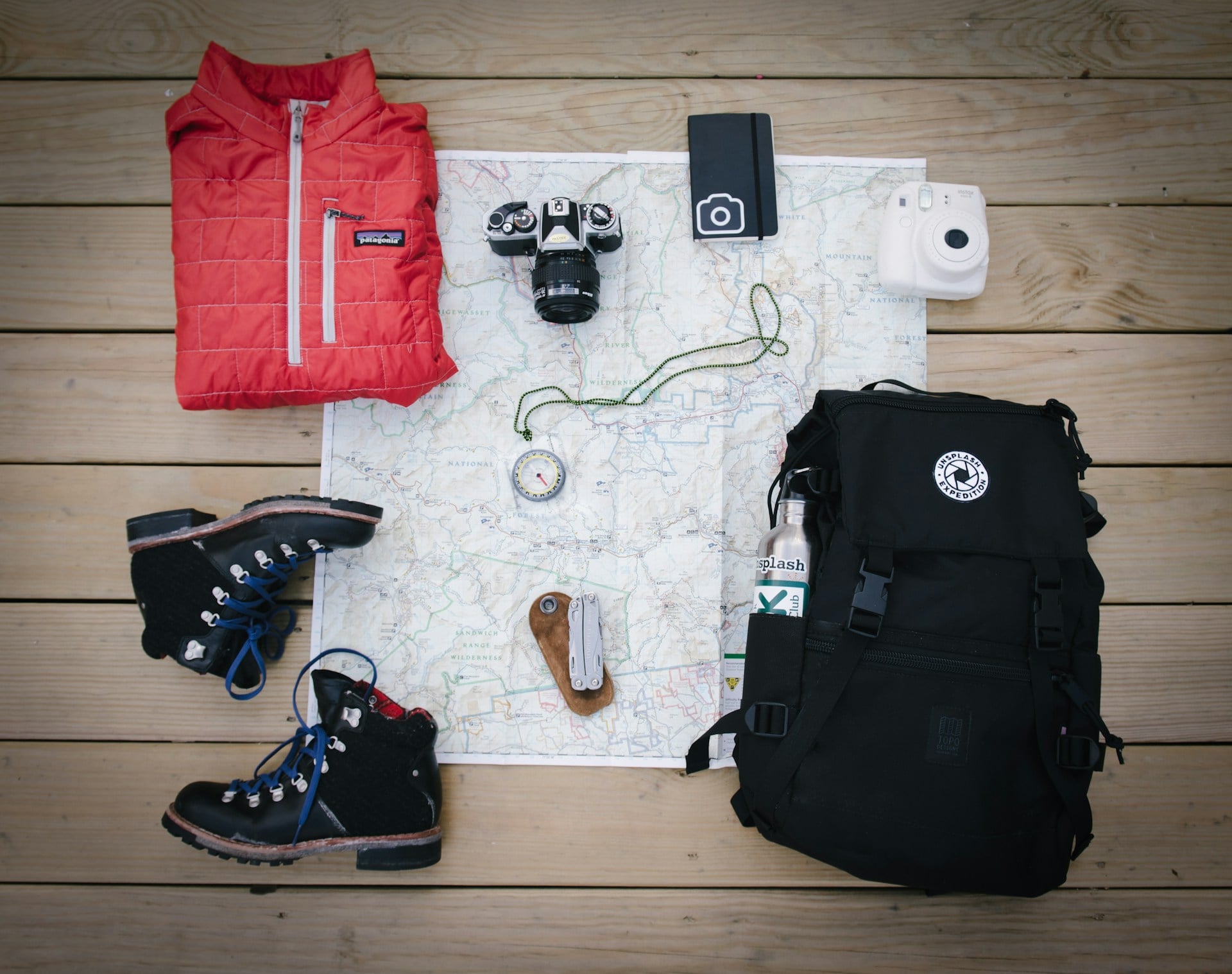 A bag, outdoor shoes, camera, map and outdoor top, folded ready to be packed.