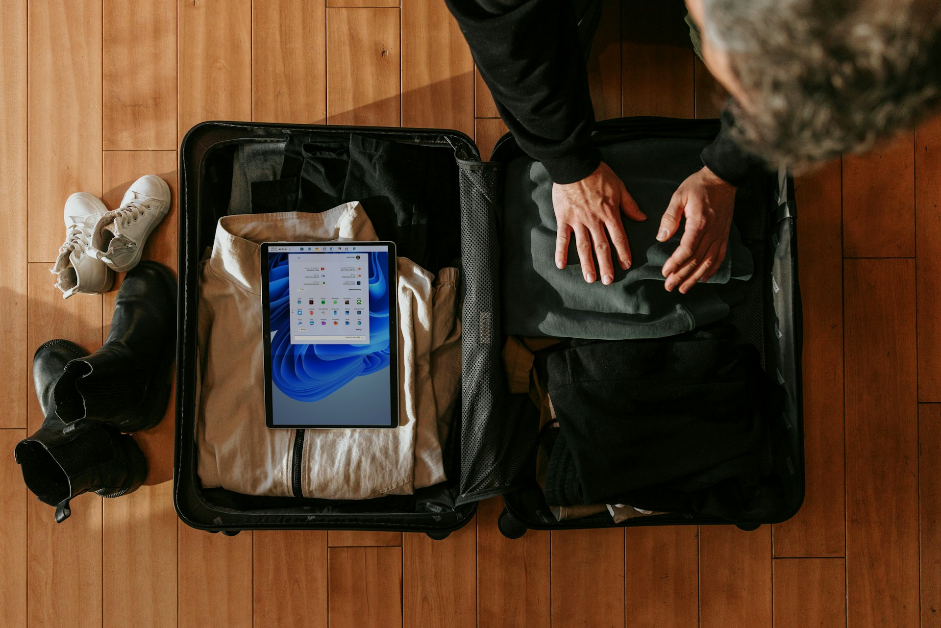 A man packing a suitcase from above. His iPad is visible packed inside a black case.